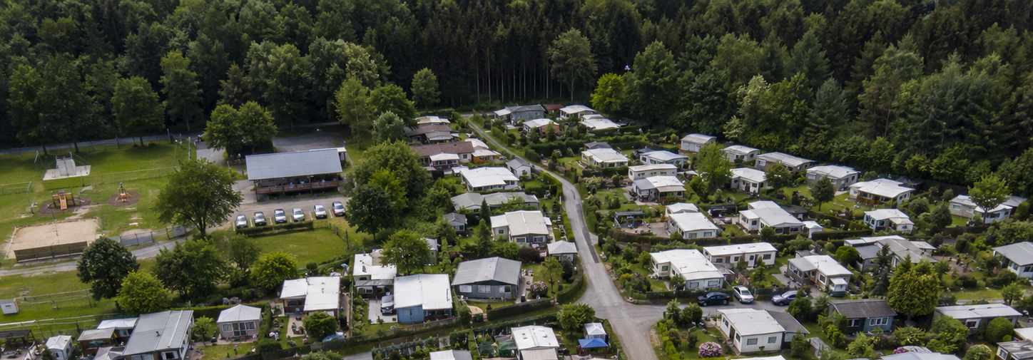 Luftaufnahme eines Dauercampingplatzes mit Wohnwagen, Vorzelten und Schutzdächern.